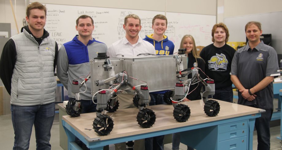 SDSU mechanical engineering students who qualified for the finals of a NASA contest are, from left, Braxton McGrath, Aiden Carstensen, graduate adviser Liam Murray, Dylan Stephens, Delaney Baumberger, Alex Schaar and faculty adviser Todd Letcher. They are pictured with a prototype of a rover designed to explore rugged, frozen lunar craters.