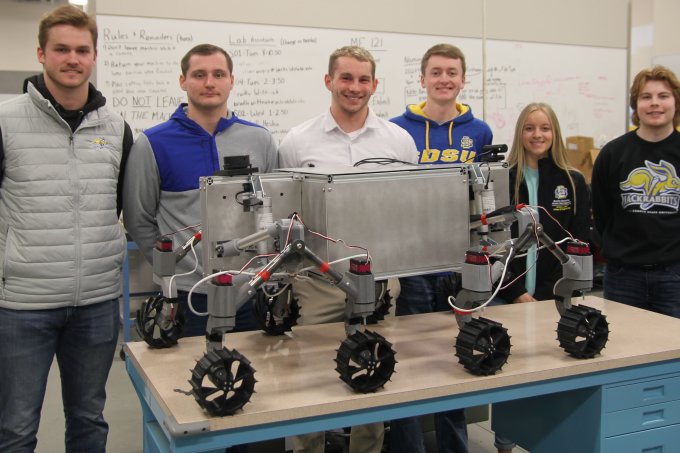 SDSU mechanical engineering students who qualified for the finals of a NASA contest are, from left, Braxton McGrath, Aiden Carstensen, graduate adviser Liam Murray, Dylan Stephens, Delaney Baumberger and Alex Schaar. They are pictured with a prototype of a rover designed to explore rugged, frozen lunar craters.