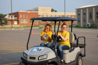Two SDSU employees ride in a golf cart for Meet State during move-in weekend on campus.
