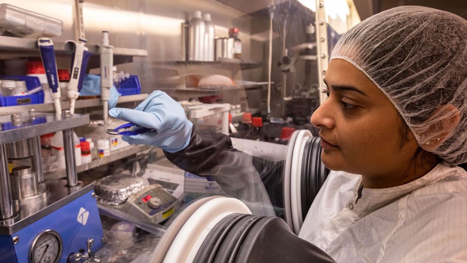 Doctoral student holding a lithium-ion battery in a tweezers in the clean room "glove box"