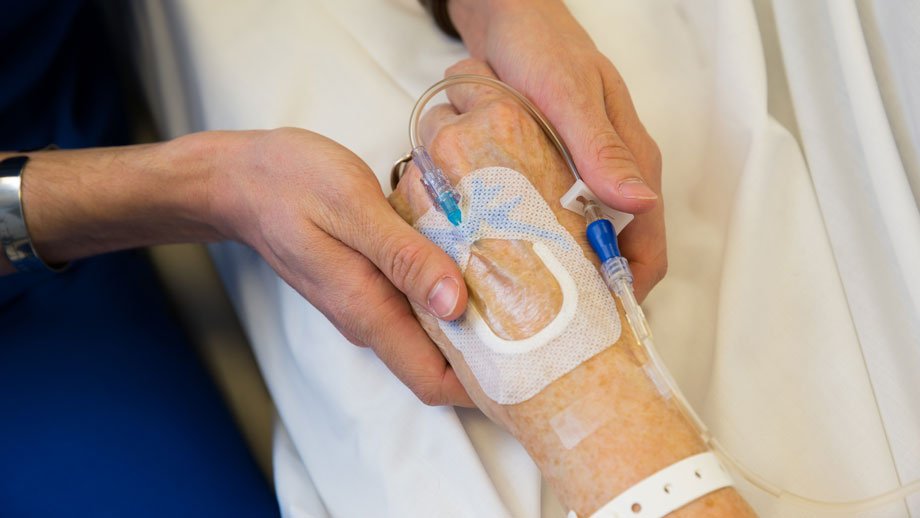nurses's hands holding a patients hand that has an IV