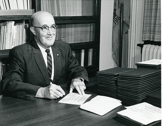 David B. Doner sitting at his desk signing diplomas