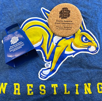 A coaster with SDSU logo, a cowbell with the SDSU logo, a blue wrestling T-shirt with a jackrabbit on it.