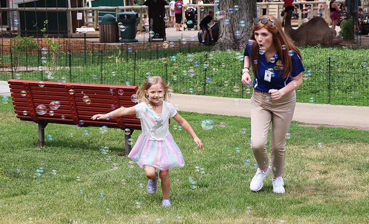 A child and an SDSU student run through bubbles at a health fair at the Great Plains Zoo in Sioux Falls on June 16.