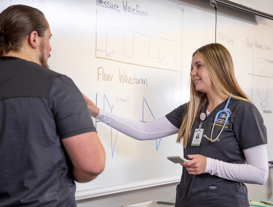 A respiratory care student works with an instructor at a white board.