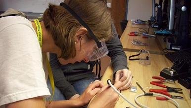 A student wearing goggles while working closely on some wiring. 
