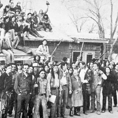 Native American activists during the Wounded Knee Occupation. A sign above the door in the background reads “Independent Oglala Nation Wounded Knee.”
