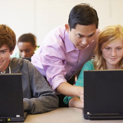 Teacher pointing at computer screen and helping a student in the classroom.
