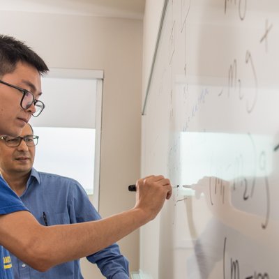 male student and male professor work at a dry erase board