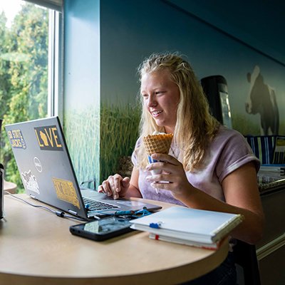 Student in front of a laptop while eating an icecream cone at the SDSU Dairy Bar