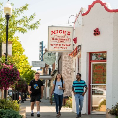 Three people walking in front of Nick's Hamburger Shop