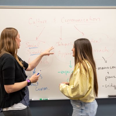 Student and instructor having a conversation in front of a whiteboard in a classroom.