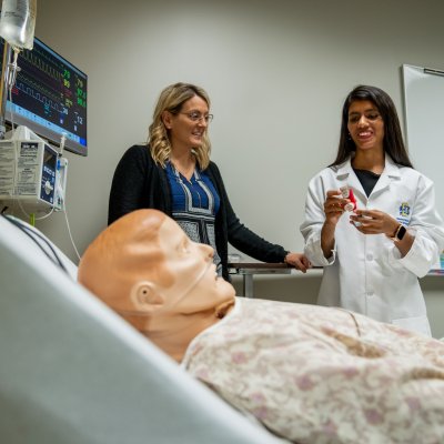 Student nurse and professor standing next to a dummy patient.