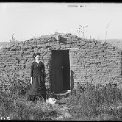a woman in front of her sod home