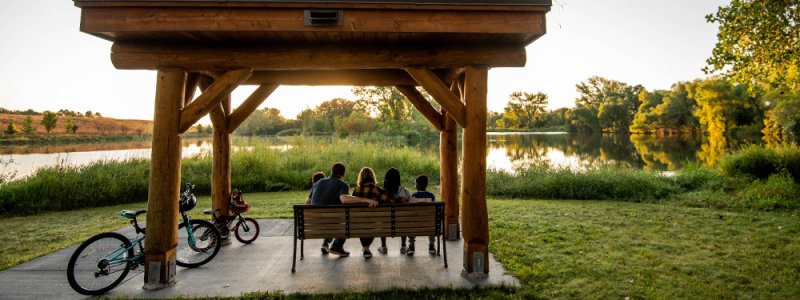 A family of five sits on a bench at a nature park
