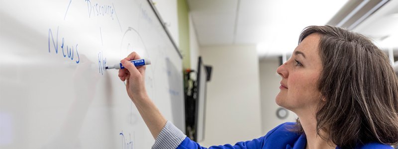 a female professor writes on a dry erase board