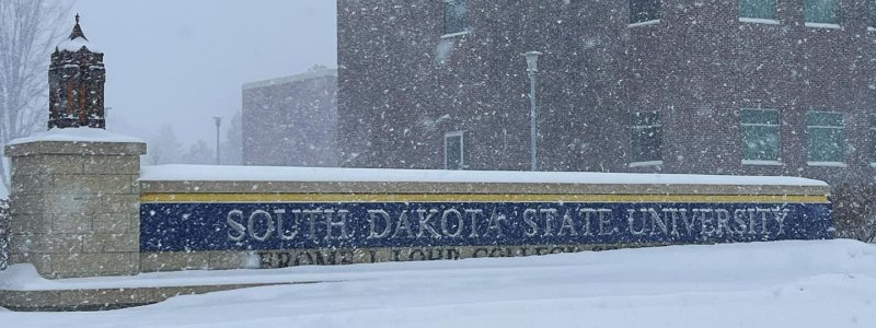 South Dakota State University sign during a 2022 winter storm with snow piled in front of it.