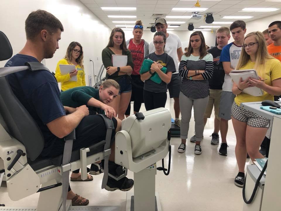Students gathered around man sitting in biodex chair with instructor teaching.