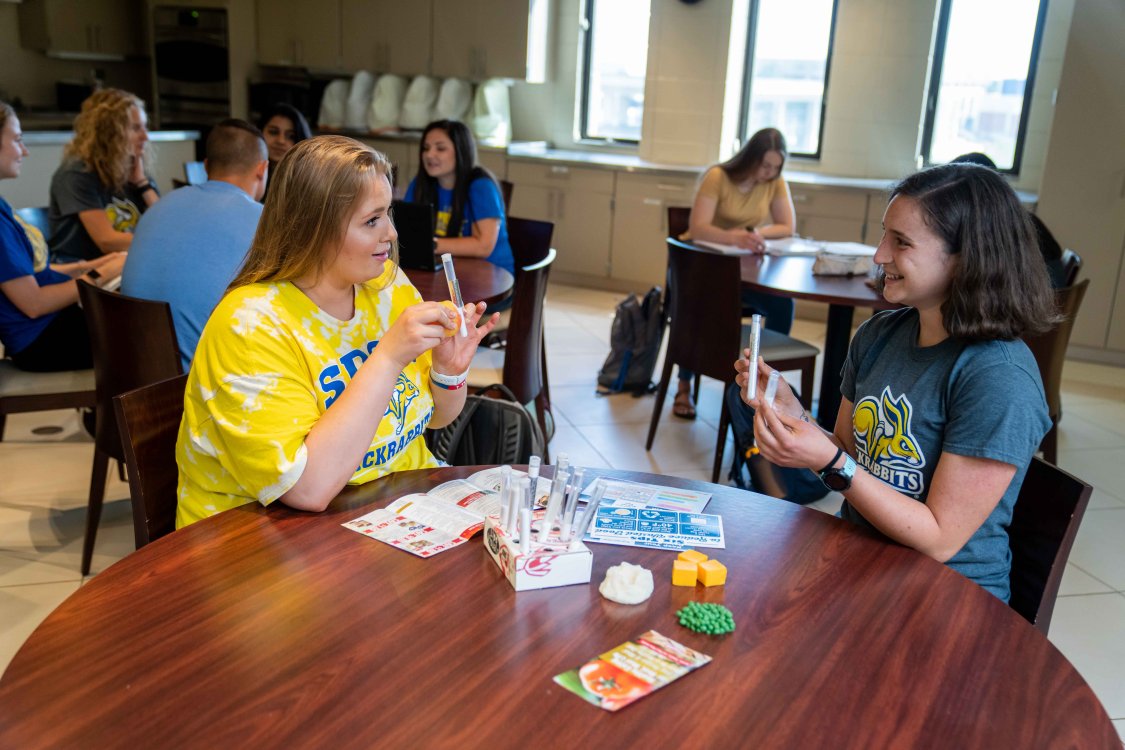 two young female students sitting at table with food models and handouts