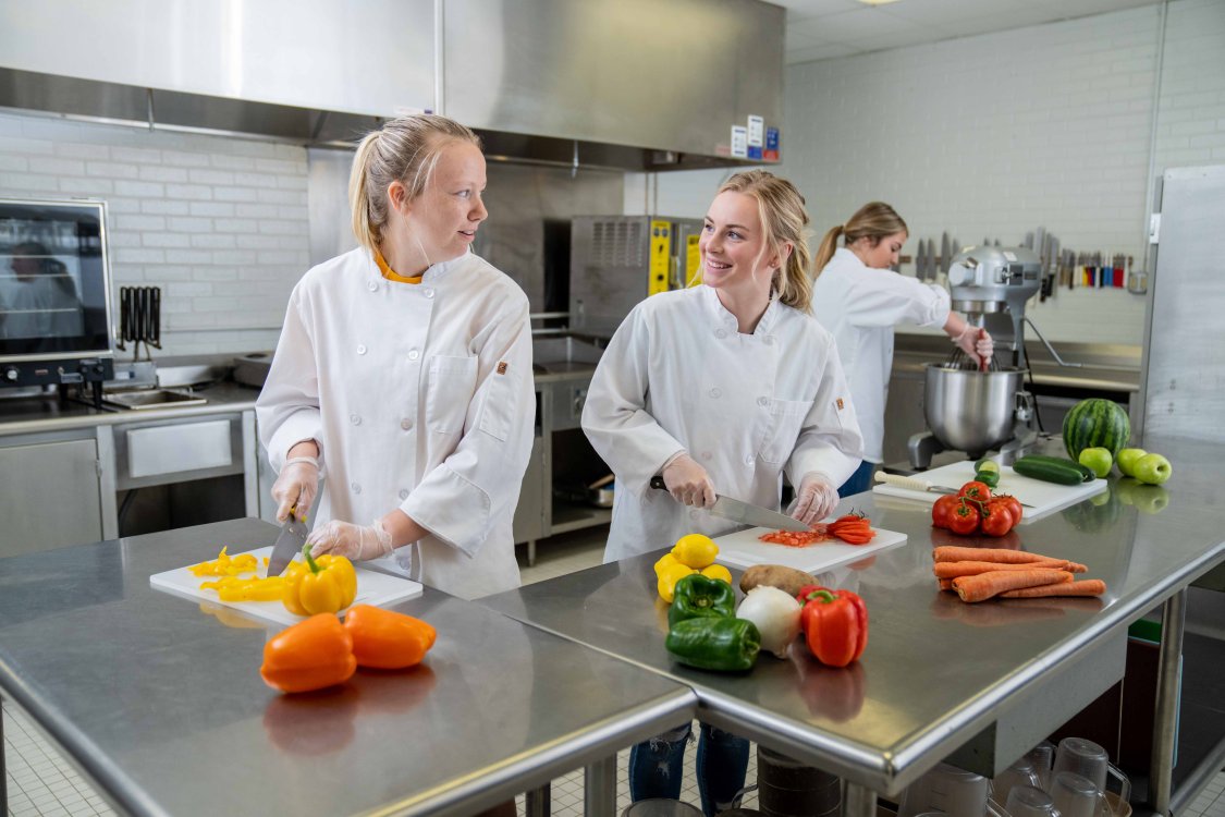 two female students in white lab coats chopping vegetables in an SDSU food lab