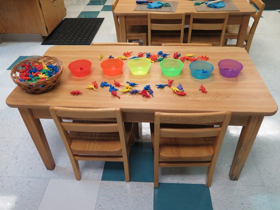 The math table has a sorting experience with colored bowls and colored dinosaurs in the 3 & 4 year old room.