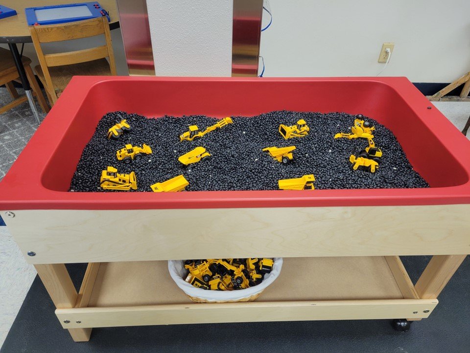 4 & 5 year old sensory table with black beans and construction vehicles.