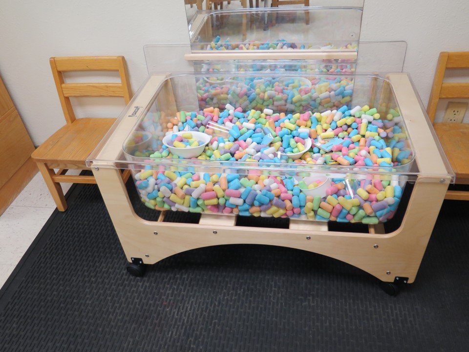 Toddler sensory table filled with colored puffs.