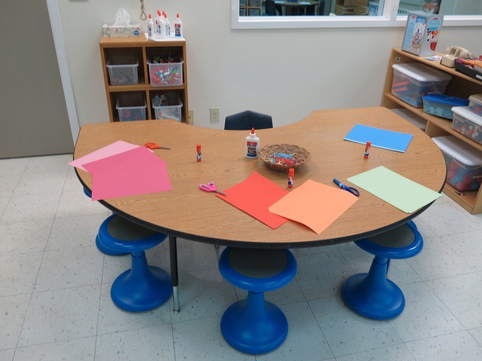 This table has a variety of papers, scissors and glue. 