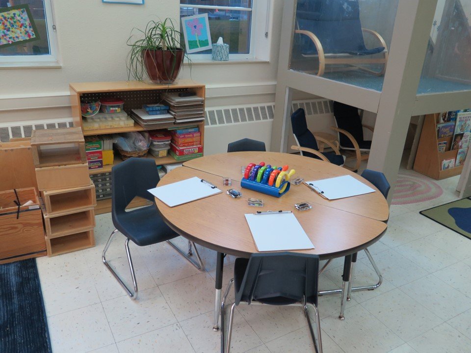 The science table in the Kindergarten classroom that includes a table with clipboards, magnifying glasses and items to examine.
