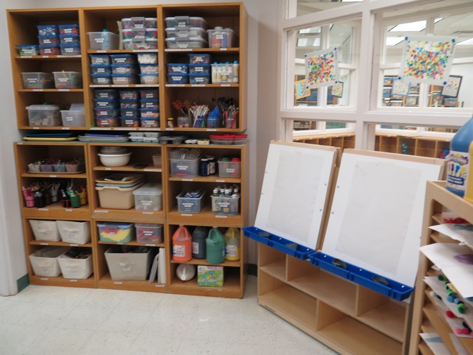 Another perspective of the Kindergarten's own art studio area. It includes a double easel and a shelving unit with art materials.