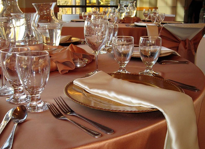 Close up of a place setting on a table with a silky bronze tablecloth, cream colored napkins, and a gold charger.