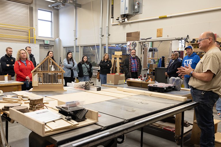 Educators standing in a shop class while a man speaks.