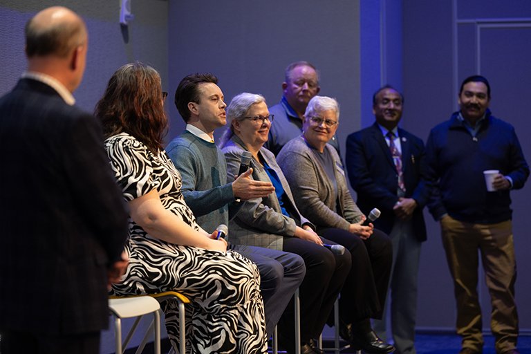 A panel of 7 people speaking on stage.