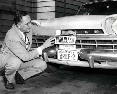 Reifel holding a 1961 SDSC Hobo Day bumper sticker by the license plates on his car