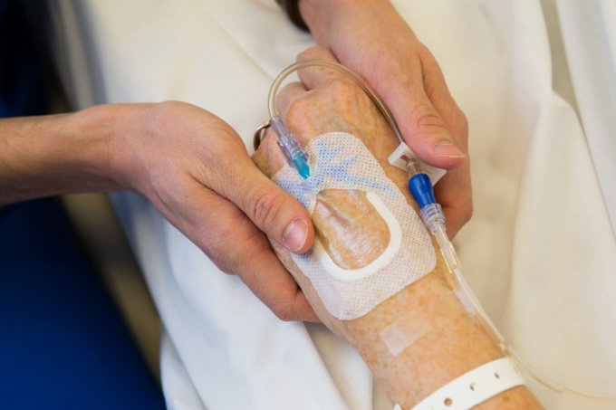 nurses's hands holding a patients hand that has an IV