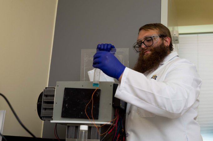 Doctoral student Kyle Birch putting test tube into prototype device