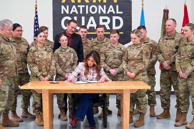 South Dakota Gov. Kristi Noem signs a bill increasing state tuition assistance for members of the South Dakota National Guard as members look on.