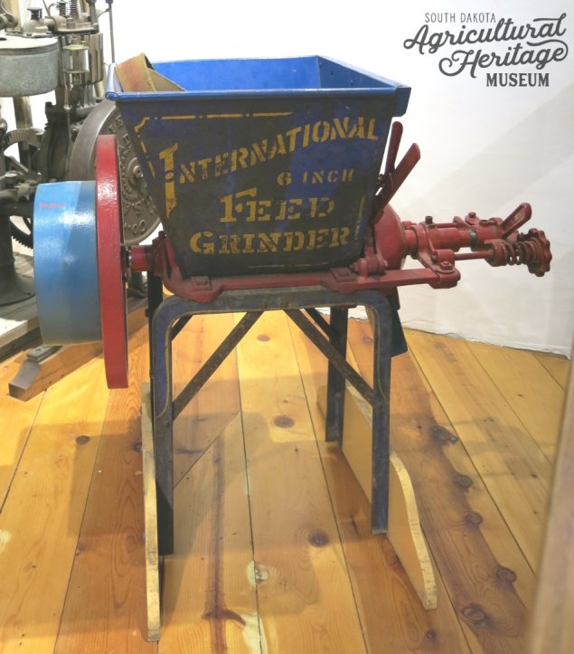 1970:018:001 Blue buhr mill on a metal platform.  Yellow printed text on one side reads "International 6 Inch Feed Grinder".