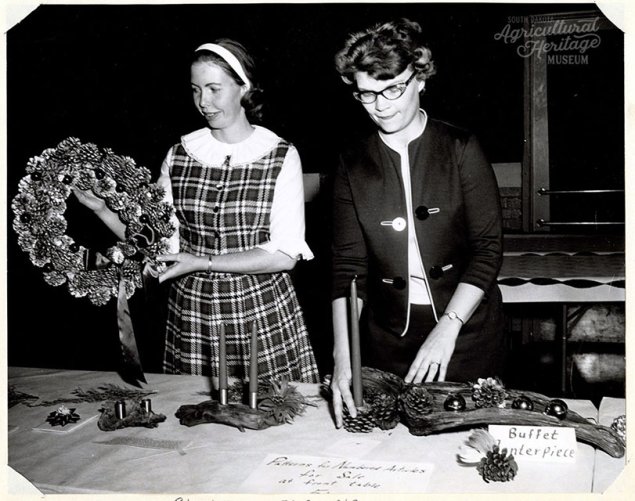 A black and white photograph of two women standing in front of a table with Christmas decorations on the table