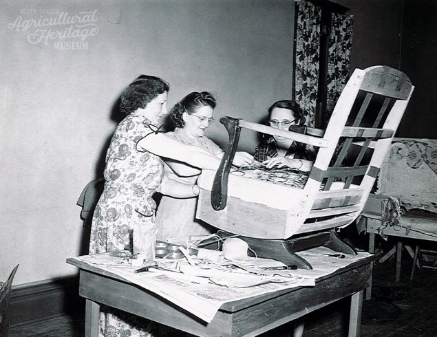 Black and white photo of three women reupholstering a chair.