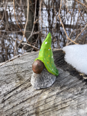Clay gnome figure with a lime green hat sitting on a log