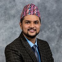 Profile photo of Sajal Bhattarai. In the photo, Mr. Bhattarai is smiling and has worn a coat, and a "dhaka topi" (dhaka topi is a cap--and is a part of the national attire of Nepal)