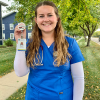 Hannah Ference stands by a tree holing her badge for clinical