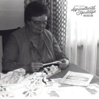 Woman sitting at kitchen table working on a hardanger (needlework) project.