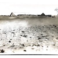 2011:040:0005 Black and white photo of a field and farmhouse.  Top soil has blown in along the fence line.