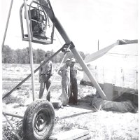 Black and white photo of three men monitoring oats being moved in an auger.