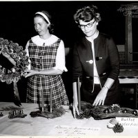 A black and white photograph of two women standing in front of a table with Christmas decorations on the table