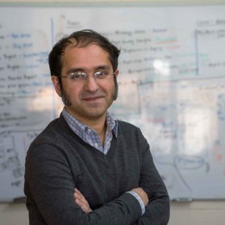 assistant professor Saikat Basu standing with arms folded in front of a white board