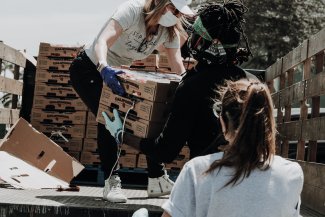 Three women unloading a truck of food and handing boxes to each other.