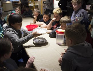 A group of young children are sitting at tap with three pie pans on it.